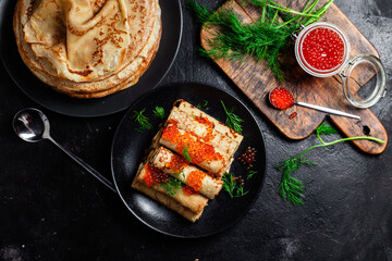 Delicious blini with red caviar in a black plate on the table. Thin pancakes. 
