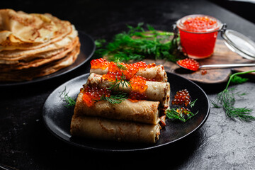 Delicious blini with red caviar in a black plate on the table. Thin pancakes. 