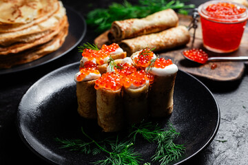 Delicious blini with red caviar in a black plate on the table. Thin pancakes. 