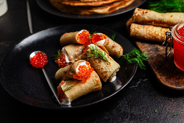 Delicious blini with red caviar in a black plate on the table. Thin pancakes. 