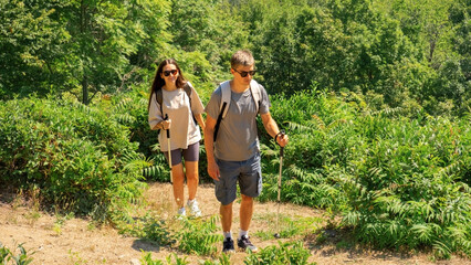 Active couple hiking together through green forest trail on a sunny summer day, enjoying adventure...