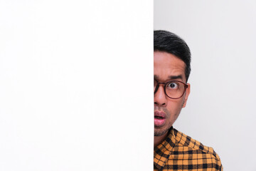 Adult Asian man face peeking from behind a wall with scared expression