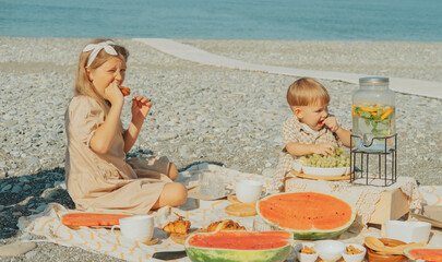Kids enjoy summer beach picnic with fresh fruits and pastries. Relaxing holiday moment by the sea...