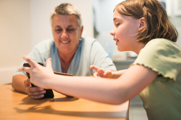 Smiling caucasian grandmother and granddaughter enjoying time together with smartphone.	