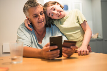 Fototapeta premium Smiling caucasian grandmother and granddaughter enjoying time together with smartphone. 