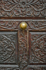 Close-up of an intricately carved wooden door with a central brass doorknob, showcasing detailed floral and scrollwork patterns