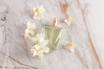 A glass transparent perfume bottle of lies on an abstract marble background with white jasmine flowers. top view. A blank bottle mockup. A copy space