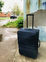 Travel suitcase resting against a weathered wall outside