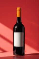 Obraz premium Elegant wine bottle with a blank label against a vibrant red backdrop, casting shadows and light.