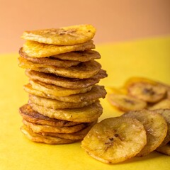 Stacked Fried Plantain Chips on Yellow Background – Crispy Tropical Snack Food Concept.
