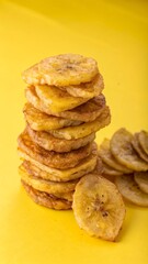 Stacked Fried Plantain Chips on Yellow Background – Crispy Tropical Snack Food Concept.