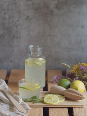 Glass bottle and glass with refreshing lemonade, wooden table, natural light and summer ingredients