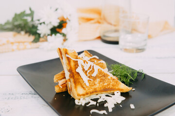 A close-up of a delectable grilled sandwich decorated with shredded cheese and fresh herbs, set against a decorative background, emphasizing a pleasant and inviting culinary presentation.