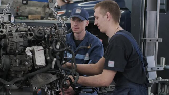 Mechanics removing engine using hoist in auto service workshop.