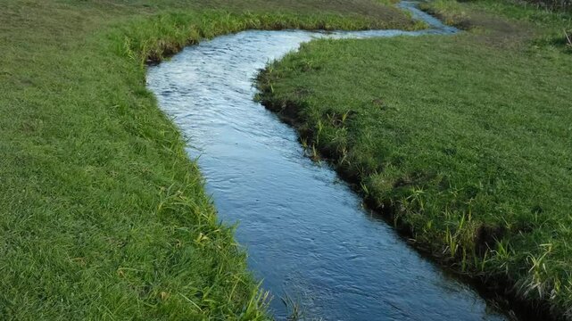 a narrow river between banks with green grass