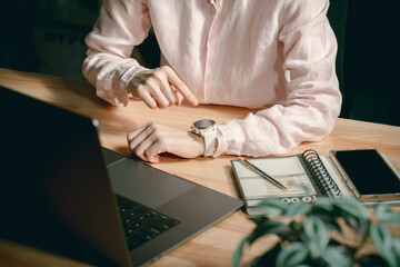 Businesswoman using white smart watch at wooden desk with laptop planner and smartphone during...