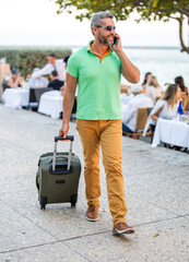 Tourist booking vacation trip. Traveler suitcase for summer trip. Man booking summer trip. Hispanic tourist traveler book online outdoor. Tourist with travel bag. Traveler using phone. Tourism app