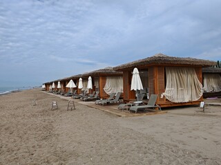 Wooden gazebo with thatched roofs, curtains, sofas with cushions, plastic deck chairs and umbrella...