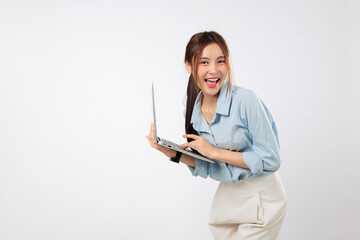 Laptop on desk as happy young Asian woman smiling types with energy, using another laptop screen...