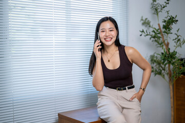 A woman is sitting on a desk and talking on her cell phone