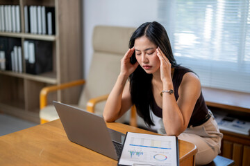 A woman is sitting at a desk with a laptop and a stack of papers