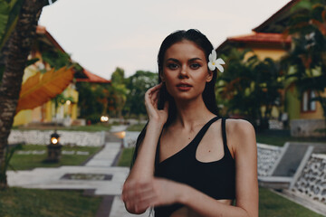 Tropical paradise Woman in black bikini top with flower in hair standing in front of palm trees