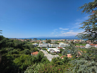 A scenic viewpoint overlooking a vibrant Greek tourist town, framed by green trees and the sea.