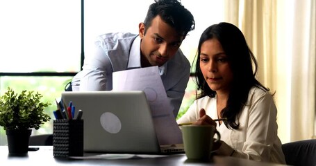 Indian business people using laptop and documents, Asian corporate man and woman in formal attire discussing reports, working together with laptop at modern indoor office desk, teamwork concept