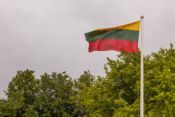 National flag of Lithuania, waving against stormy gray sky, blowing in the wind in city park
