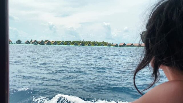 Woman Tourist on boat admire Maldives island resort with water villas on sunny day tropical seascape