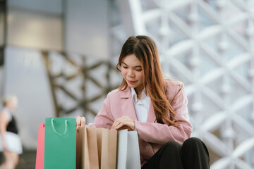Happy young Asian woman shopping in a modern city during the evening, carrying bags, smiling,...