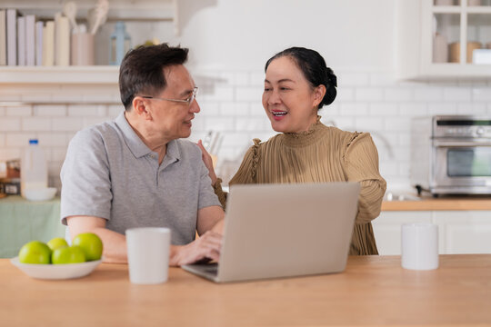 Asian senior couple sitting at the kitchen dining table, smiling warmly as they video call their grandson to celebrate his birthday online. Embracing technology, the grandparents use a digital tablet - Powered by Adobe