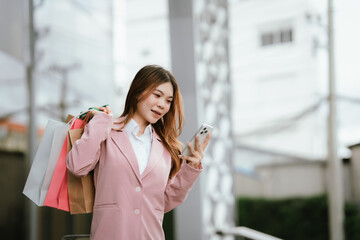Happy young Asian woman shopping in a modern city during the evening, carrying bags, smiling,...