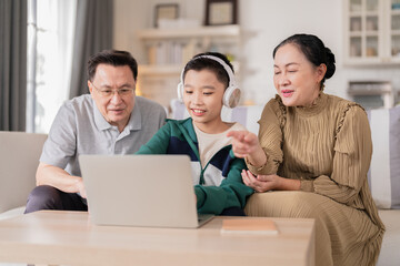 Grandparents and grandson spending quality time together at home while the elderly grandfather and grandmother support their young grandson with school homework and digital learning on a laptop