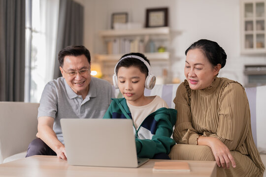 Grandparents and grandson spending quality time together at home while the elderly grandfather and grandmother support their young grandson with school homework and digital learning on a laptop