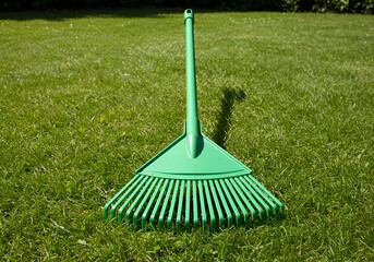 Top view of a green plastic rake on freshly mowed grass with symmetrical composition, bright daylight.