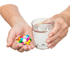 A senior Caucasian woman holds a handful of colorful pills in one hand and a glass of water in the other. The background is transparent.
