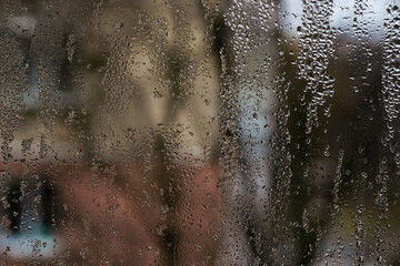 drops cling to cold inside window surface, some merging into winding streams while others remain...