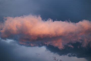nuvola colorata di arancione dalla luce del sole al tramonto, in primo piano, con nuvole color blu scuro sullo sfondo
