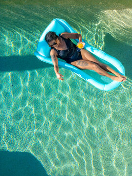 Woman relaxing in pool on float with drink in hand