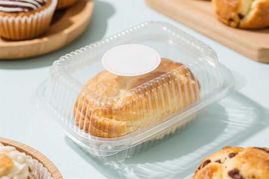 A clear plastic clamshell container with a golden baked good inside is placed on a light blue surface. This container is perfect for branding and can be used for food and dessert packaging.