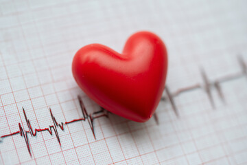 Red heart on cardiogram paper symbolizes heart health and medical care, showing static heartbeat and cardiovascular wellness in a clinical setting with clear medical chart lines.