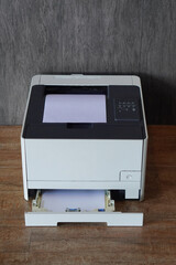 top view  black and white laser printer sitting on a wooden floor. A stack of white paper is...