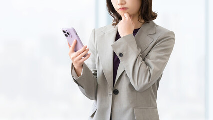 スマートフォンを見て考える女性・ビジネスウーマン