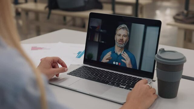 Portrait of businessman communicating with colleague via video call laptop screen view. Young woman listens to boss during video-chat in cafeteria closeup. Business meeting