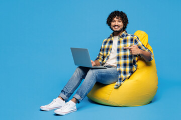 Full body young happy Indian IT man wear yellow checkered shirt casual clothes sit in bag chair...