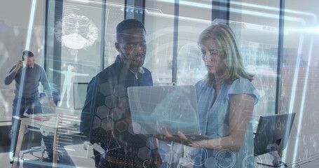 Collaborating pair of tech pros examining laptop in open plan office, with brain-scan overlays
