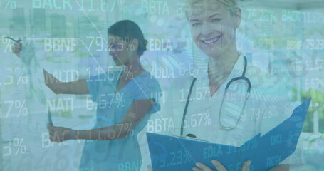 Holding clipboard, smiling doctor examining X-ray in clinic with stock data overlay, copy space