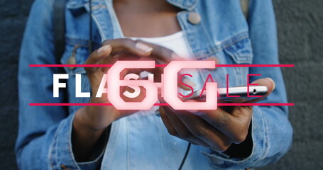 Holding smartphone woman wearing denim jacket against urban grey wall, with neon Flash Sale graphic