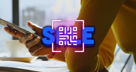 Woman in yellow top holding smartphone at desk by window, with neon QR code spelling SCAN